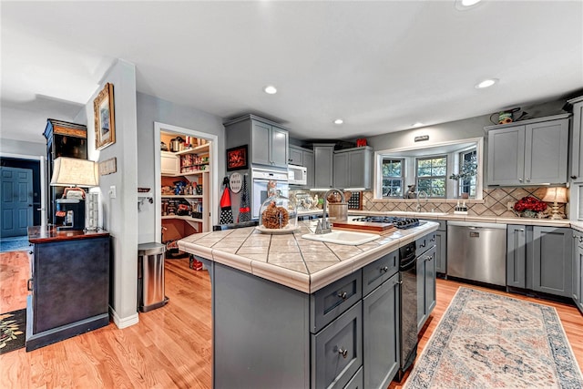 kitchen featuring appliances with stainless steel finishes, light hardwood / wood-style floors, tile countertops, a center island, and gray cabinets