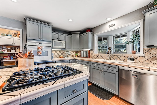 kitchen with appliances with stainless steel finishes, backsplash, light hardwood / wood-style flooring, and gray cabinetry