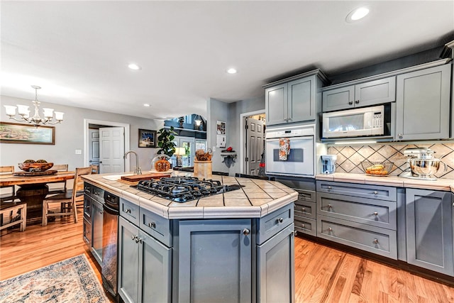 kitchen with white appliances, a kitchen island with sink, sink, pendant lighting, and light hardwood / wood-style flooring