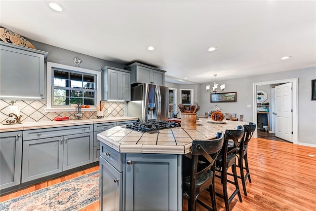 kitchen with a center island, black gas cooktop, stainless steel fridge, light wood-type flooring, and decorative light fixtures