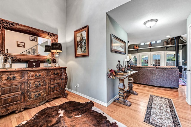 hallway with french doors, light wood-type flooring, and a textured ceiling