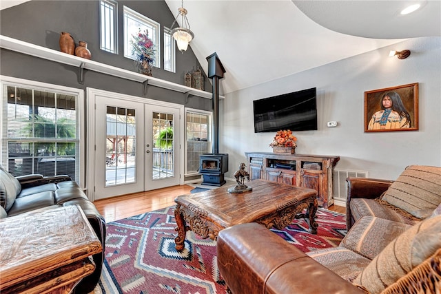 living room with hardwood / wood-style floors, high vaulted ceiling, a wood stove, and french doors