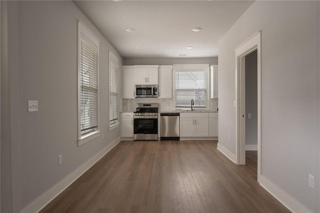 kitchen featuring backsplash, sink, hardwood / wood-style flooring, white cabinetry, and stainless steel appliances