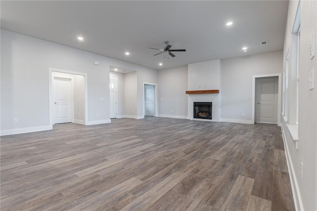 unfurnished living room with hardwood / wood-style flooring, ceiling fan, and a large fireplace