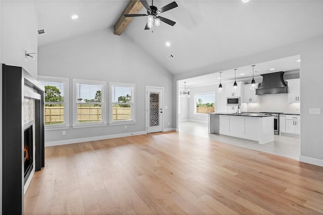 unfurnished living room featuring beam ceiling, a healthy amount of sunlight, ceiling fan with notable chandelier, and light hardwood / wood-style floors