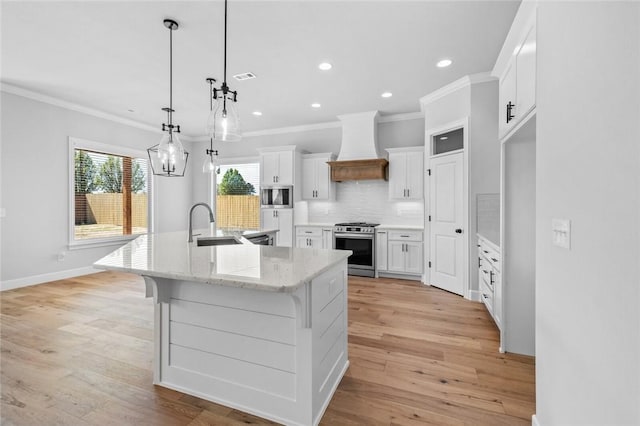 kitchen with a large island with sink, hanging light fixtures, custom range hood, white cabinetry, and stainless steel appliances