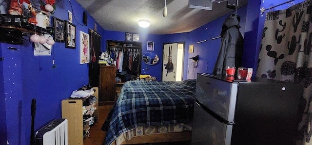 bedroom featuring radiator, a textured ceiling, and stainless steel refrigerator