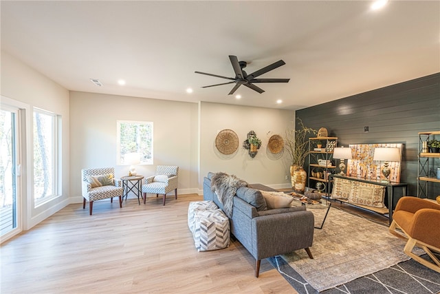 living room featuring ceiling fan, wooden walls, and light hardwood / wood-style flooring