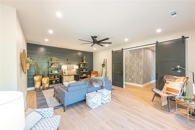 living room with light hardwood / wood-style floors, a barn door, and ceiling fan