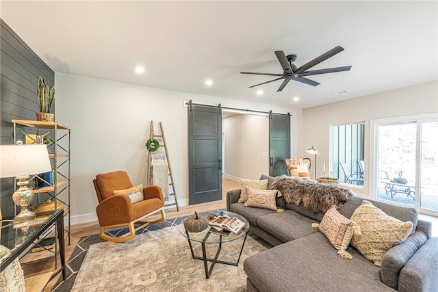 living room with wood-type flooring, a barn door, and ceiling fan