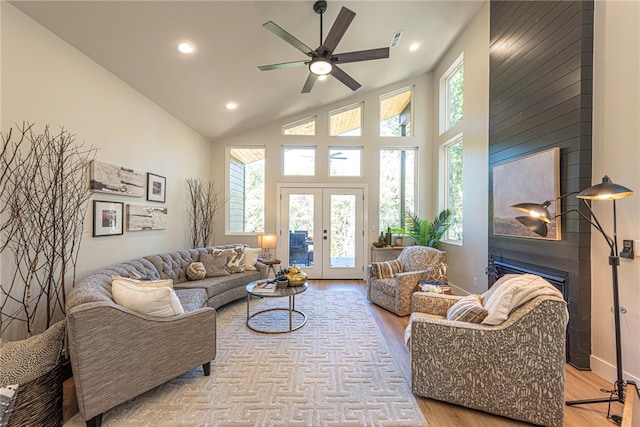 living room with high vaulted ceiling, a fireplace, ceiling fan, light wood-type flooring, and french doors