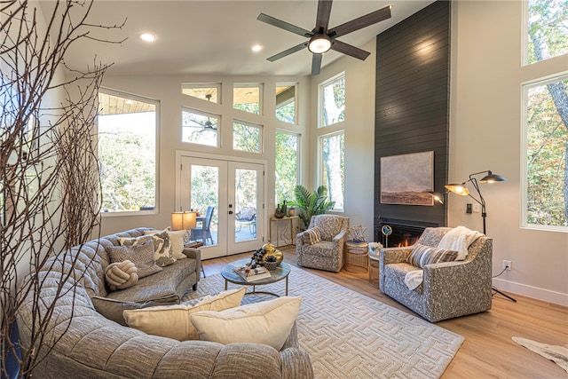 living room with french doors, a towering ceiling, a fireplace, and light hardwood / wood-style flooring