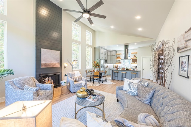 living room featuring ceiling fan, a fireplace, high vaulted ceiling, and light wood-type flooring