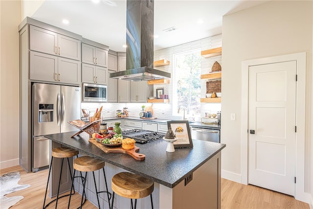 kitchen with appliances with stainless steel finishes, a kitchen breakfast bar, a center island, and island range hood