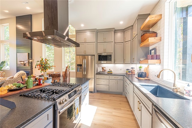 kitchen with sink, light hardwood / wood-style flooring, appliances with stainless steel finishes, island exhaust hood, and decorative backsplash