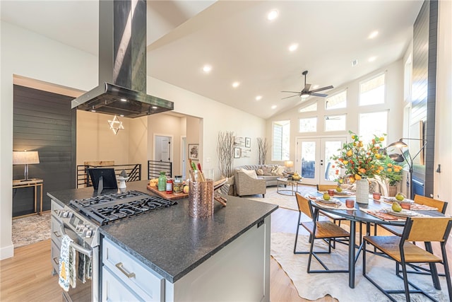 kitchen with high vaulted ceiling, stainless steel range with gas cooktop, island exhaust hood, light hardwood / wood-style floors, and white cabinets