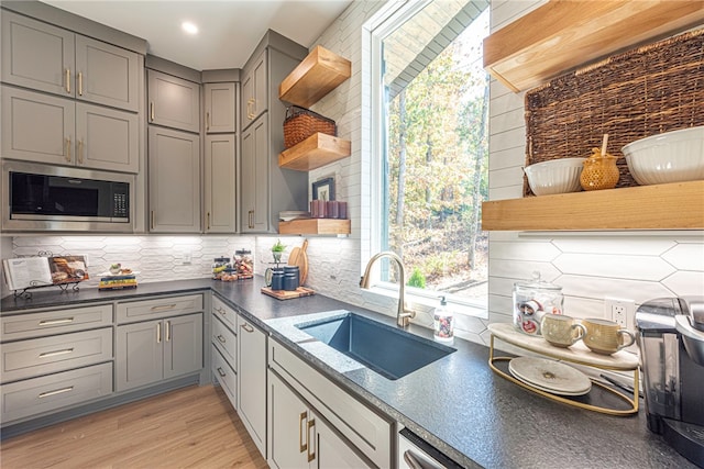 kitchen featuring sink, gray cabinetry, light hardwood / wood-style floors, built in microwave, and decorative backsplash