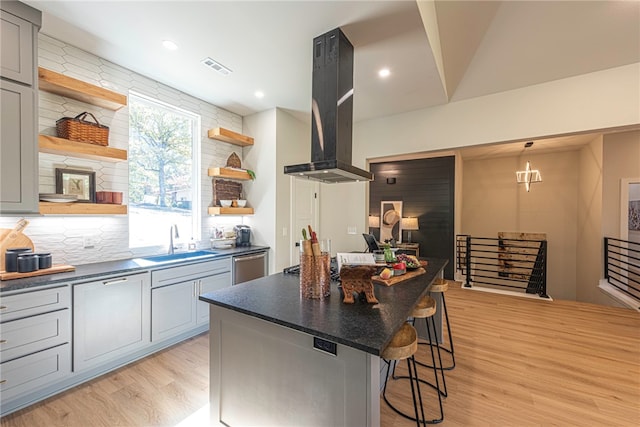 kitchen with sink, gray cabinets, a breakfast bar, a kitchen island, and island exhaust hood