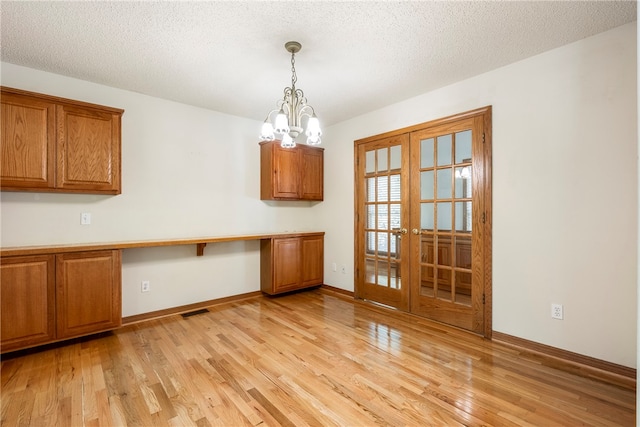 unfurnished dining area featuring a textured ceiling, light wood-type flooring, and a notable chandelier