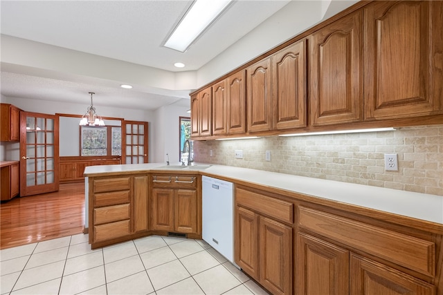 kitchen with sink, an inviting chandelier, kitchen peninsula, white dishwasher, and decorative light fixtures