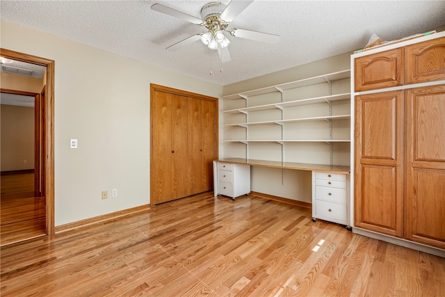 interior space with a textured ceiling, built in desk, light hardwood / wood-style flooring, and ceiling fan