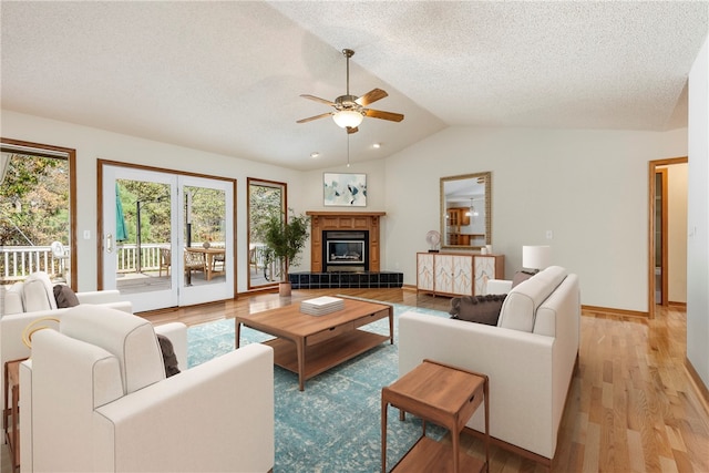 living room featuring light hardwood / wood-style flooring, vaulted ceiling, ceiling fan, a textured ceiling, and a fireplace