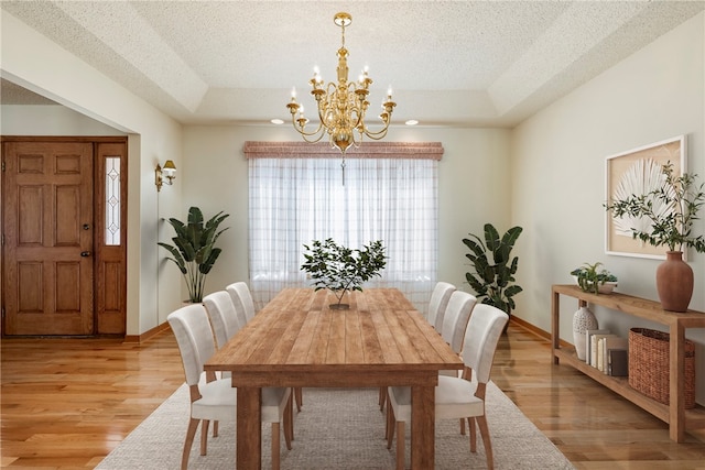 dining room featuring a notable chandelier, light hardwood / wood-style floors, a raised ceiling, and a textured ceiling