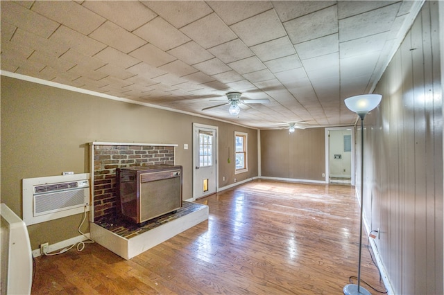 unfurnished living room featuring a wall unit AC, hardwood / wood-style flooring, ornamental molding, a brick fireplace, and ceiling fan