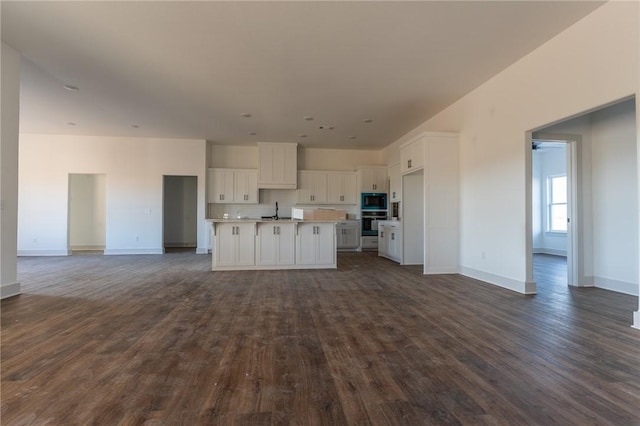 kitchen featuring backsplash, black microwave, a kitchen island with sink, sink, and white cabinetry