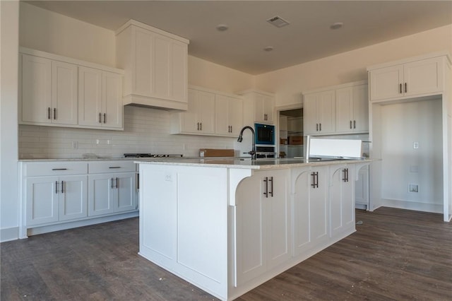 kitchen with white cabinetry, a kitchen island with sink, dark hardwood / wood-style flooring, a breakfast bar area, and decorative backsplash