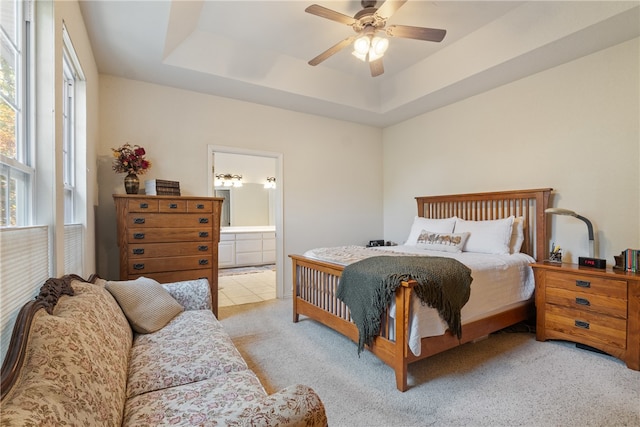 carpeted bedroom featuring ceiling fan, ensuite bath, and a tray ceiling