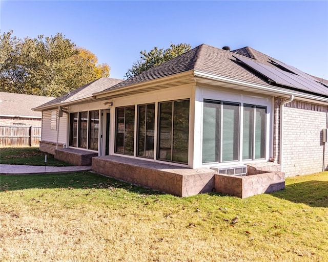 rear view of house featuring a sunroom, a lawn, and solar panels