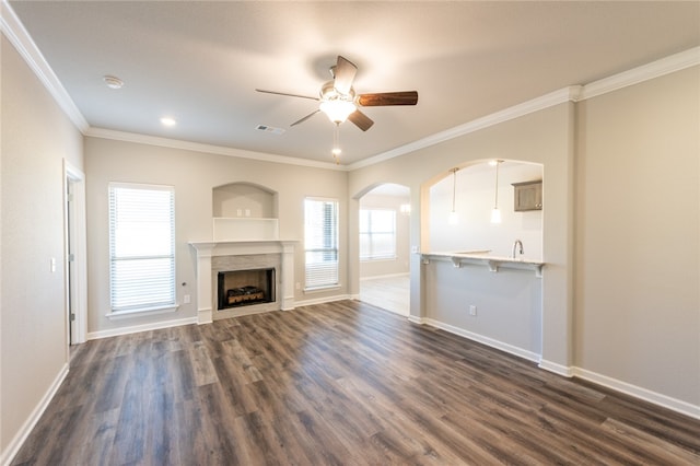 unfurnished living room with built in shelves, dark wood-type flooring, crown molding, and ceiling fan