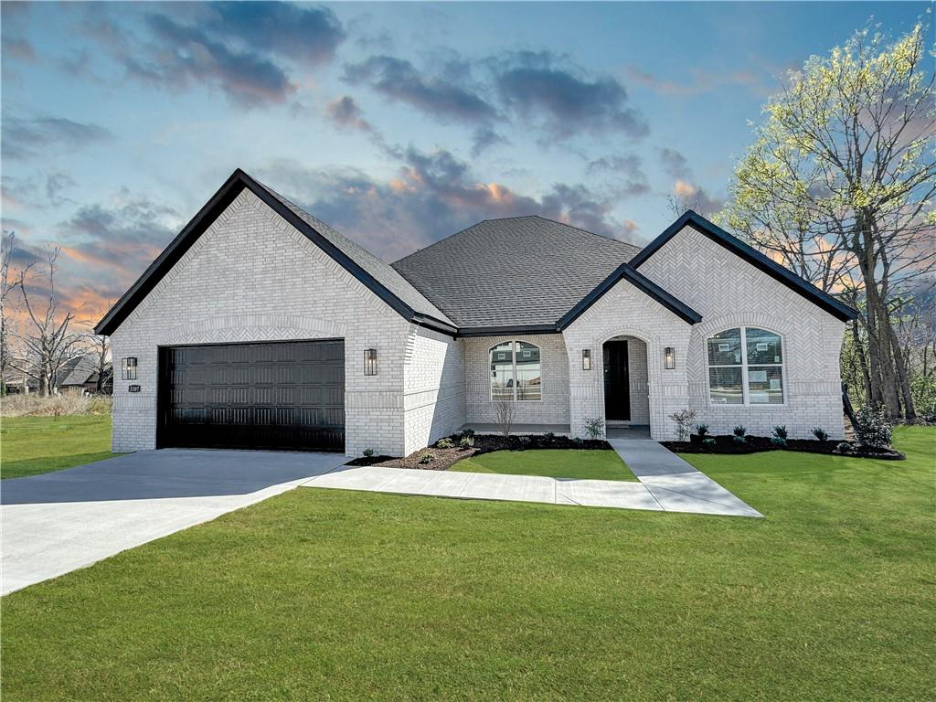 french country inspired facade with brick siding, an attached garage, a front yard, and driveway