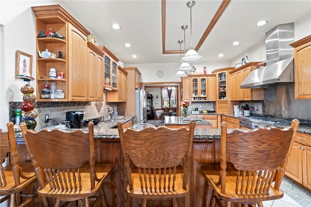 kitchen featuring wall chimney range hood, kitchen peninsula, a kitchen breakfast bar, stainless steel appliances, and light stone counters