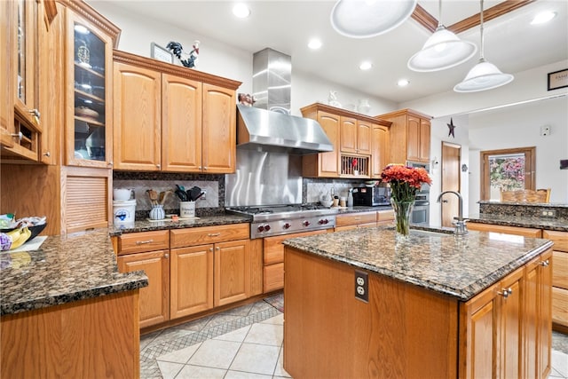 kitchen featuring stainless steel gas cooktop, a kitchen island with sink, decorative light fixtures, and dark stone counters