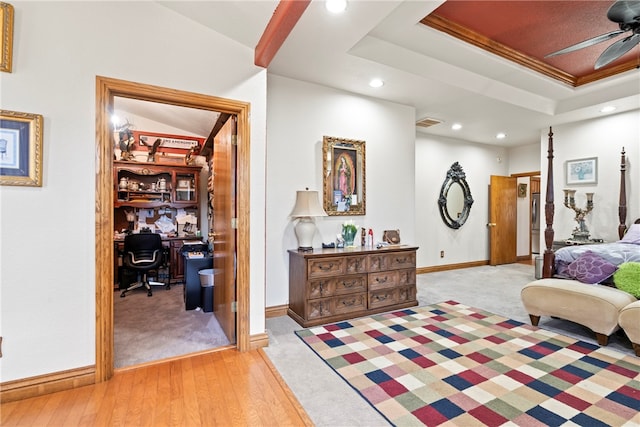 bedroom with crown molding, a tray ceiling, light wood-type flooring, and ceiling fan