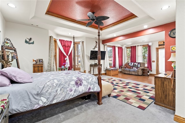 carpeted bedroom with ceiling fan, a raised ceiling, and ornamental molding