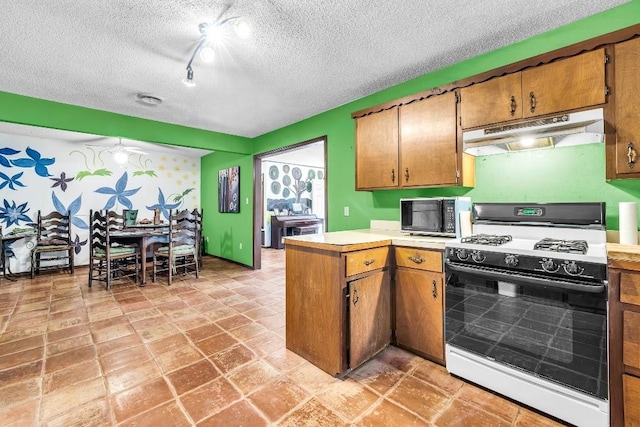 kitchen with under cabinet range hood, a textured ceiling, a peninsula, light countertops, and gas range