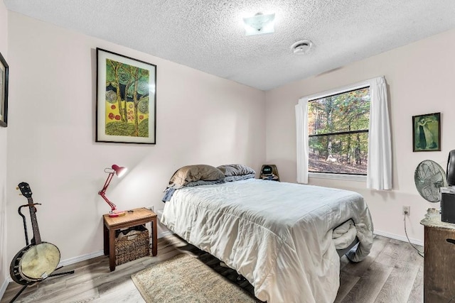 bedroom with wood finished floors, baseboards, and a textured ceiling