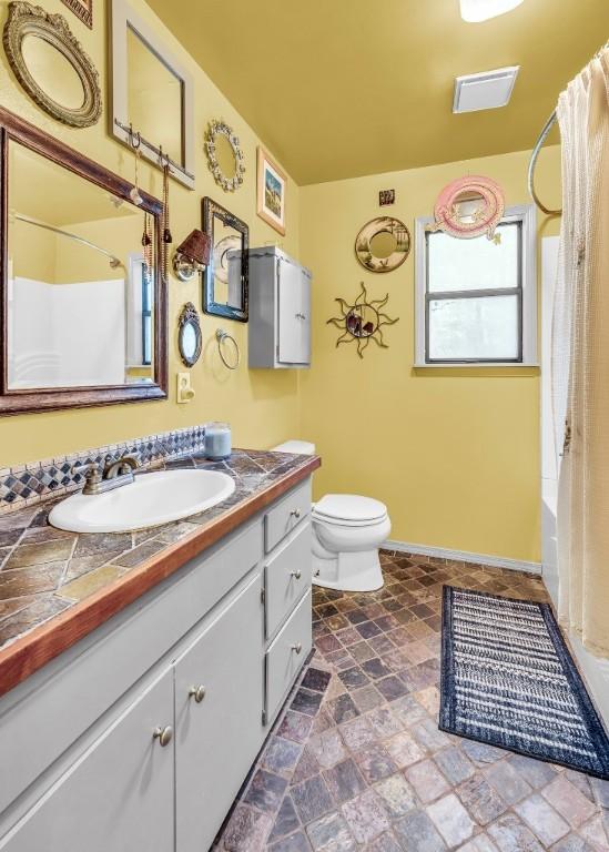 bathroom with baseboards, shower / bath combo with shower curtain, toilet, stone finish floor, and vanity