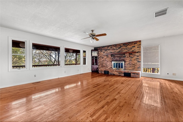 unfurnished living room featuring hardwood / wood-style flooring, ceiling fan, a textured ceiling, and a brick fireplace