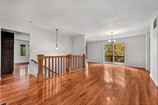 spare room featuring light hardwood / wood-style floors, a textured ceiling, and an inviting chandelier