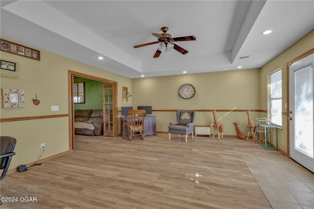 sitting room with french doors, ceiling fan, a tray ceiling, and light wood-type flooring