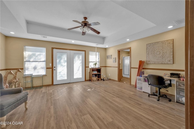 office with french doors, built in desk, a tray ceiling, light hardwood / wood-style floors, and ceiling fan