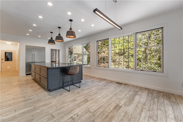 kitchen with light wood-type flooring, a kitchen island, hanging light fixtures, stainless steel built in fridge, and a breakfast bar area