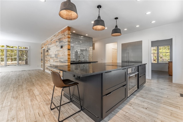 kitchen with a kitchen bar, a kitchen island, hanging light fixtures, stainless steel appliances, and light hardwood / wood-style flooring