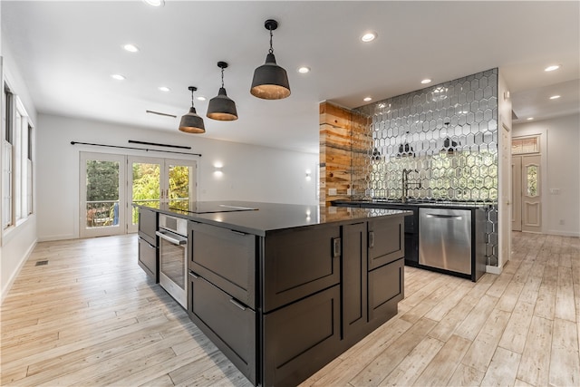 kitchen with backsplash, a center island, decorative light fixtures, appliances with stainless steel finishes, and light hardwood / wood-style floors