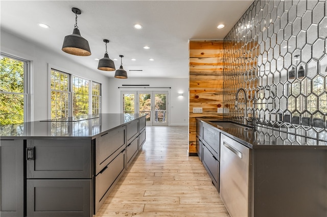 kitchen with wood walls, sink, decorative light fixtures, stainless steel dishwasher, and light hardwood / wood-style flooring