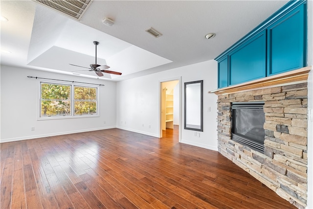 unfurnished living room featuring dark hardwood / wood-style floors, a tray ceiling, a fireplace, and ceiling fan